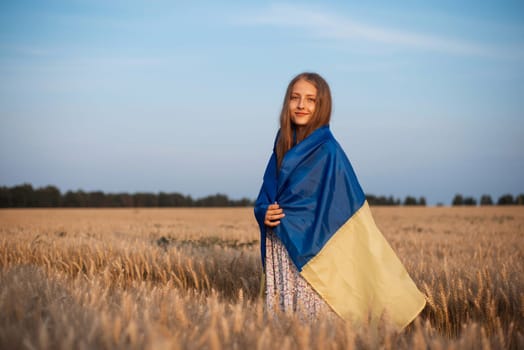 Portrait of a young girl with Ukrainian flag in the field of ripe rye