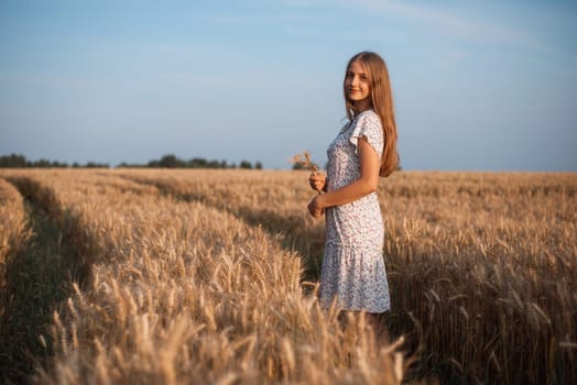 Side photo of a beautiful girl with blond hair holding spikelets of ripe rye looking to the camera