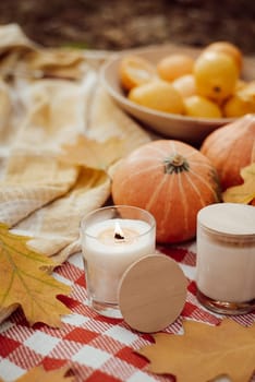 Autumn composition: candles, pumpkins, bright yellow leaves, bowl of oranges on warm plaid