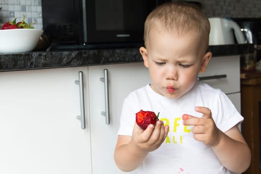 A small, bald boy is not neatly and appetizingly eating red, juicy strawberries