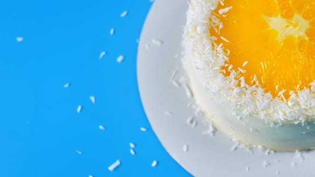 Cake with orange and coconut shavings spinning on a blue background