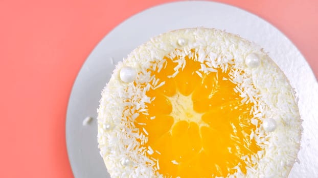 Cake with orange and coconut shavings spun on a pink background