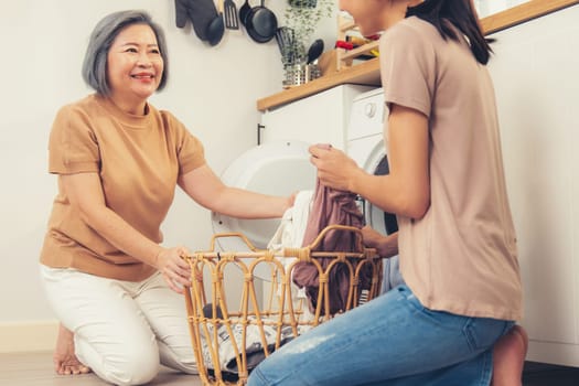 Daughter and mother working together to complete their household chores near the washing machine in a happy and contented manner. Mother and daughter doing the usual tasks in the house.