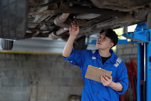 Vehicle service maintenance asian man checking under car condition in garage. Automotive mechanic maintenance checklist document. Car repair service concept.