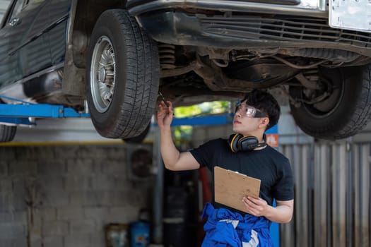 Vehicle service maintenance asian man checking under car condition in garage. Automotive mechanic maintenance checklist document. Car repair service concept.