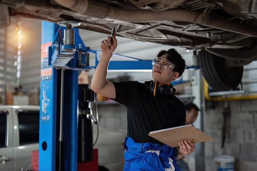 Vehicle service maintenance asian man checking under car condition in garage. Automotive mechanic maintenance checklist document. Car repair service concept.