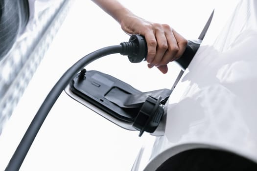 Closeup progressive man holding EV charger plug from public charging station for electric vehicle with background of residential building as concept eco-friendly sustainability energy car concept.