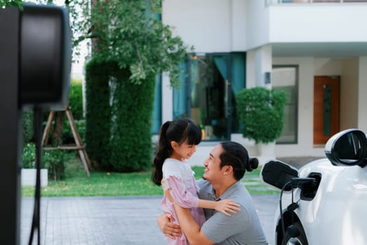 Progressive father and daughter returned from school in electric vehicle that is being charged at home. Electric vehicle driven by renewable clean energy. Home charging station concept for environment