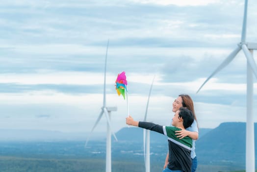 A progressive mother and her son are on vacation, enjoying the natural beauty of a lake at the bottom of a hill while the boy carries a toy windmill.