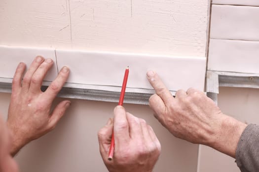 Stylish trendy white ceramic tiles on the kitchen wall. Hands in the process of laying white rectangular tiles on the bathroom wall. Renovation of apartments and bathrooms