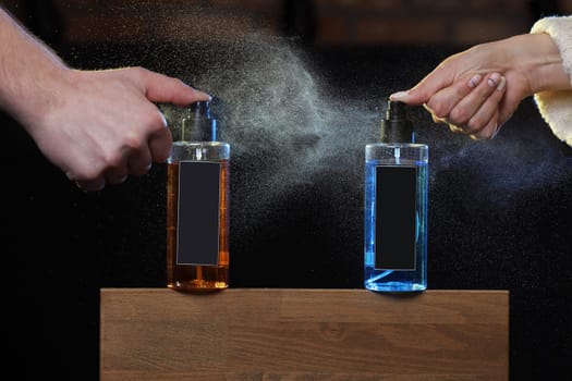 the hands of a man and a woman spray a colored hair lotion. two spray cans on black background on wooden stand. copy space on cans, jars. selective focus. barbershop.