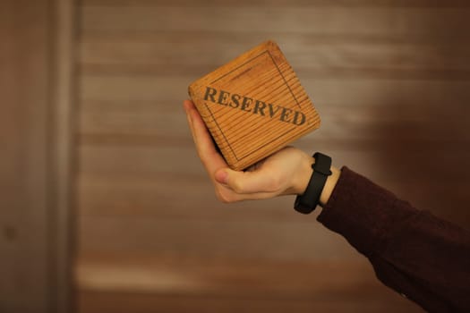 A wooden plaque has a word reserved . male hand holds a wooden plate with the inscription reserved isolated on a white background. selective focus