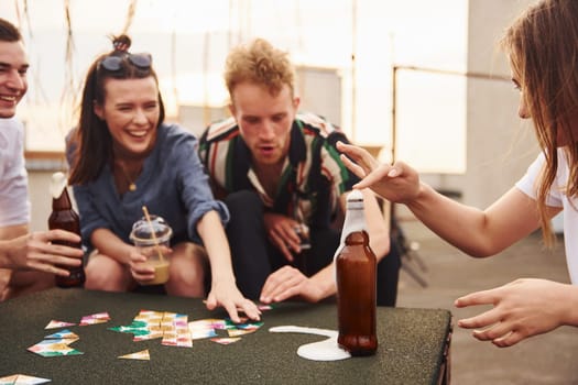 Playing card game. Group of young people in casual clothes have a party at rooftop together at daytime.