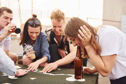 Playing card game. Group of young people in casual clothes have a party at rooftop together at daytime.