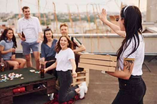 With delicious pizza. Group of young people in casual clothes have a party at rooftop together at daytime.