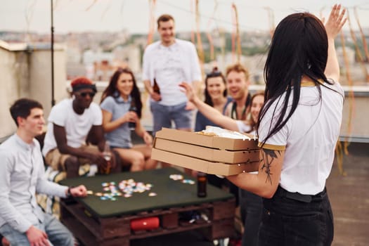 With delicious pizza. Group of young people in casual clothes have a party at rooftop together at daytime.