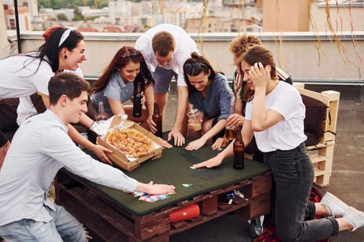 With delicious pizza. Group of young people in casual clothes have a party at rooftop together at daytime.