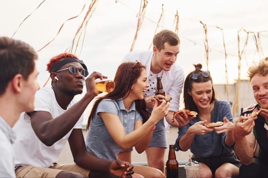 With delicious pizza. Group of young people in casual clothes have a party at rooftop together at daytime.