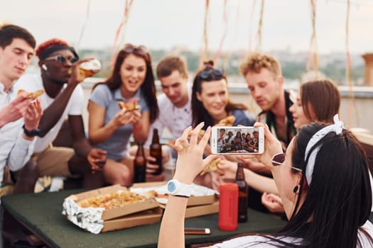 With delicious pizza. Group of young people in casual clothes have a party at rooftop together at daytime.