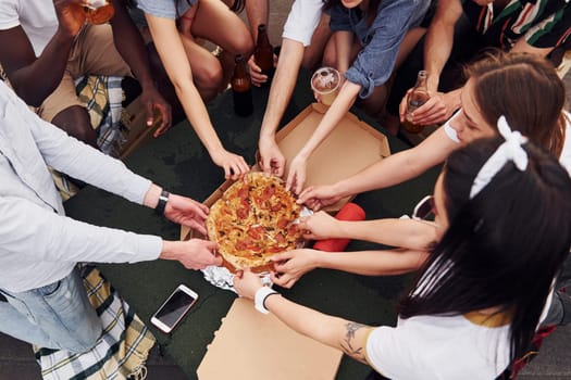 With delicious pizza. Group of young people in casual clothes have a party at rooftop together at daytime.