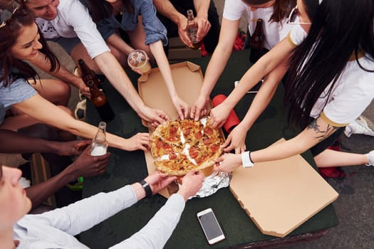 With delicious pizza. Group of young people in casual clothes have a party at rooftop together at daytime.