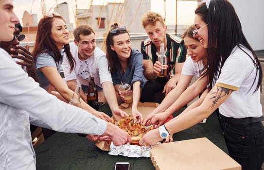 With delicious pizza. Group of young people in casual clothes have a party at rooftop together at daytime.