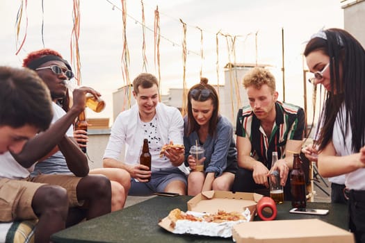 With delicious pizza. Group of young people in casual clothes have a party at rooftop together at daytime.