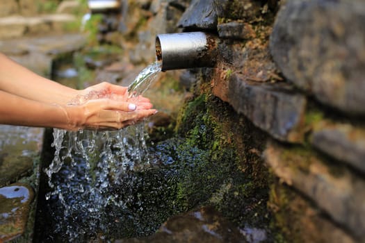 Woman collect pure water in hand palm from the source in the wall, hold and drink it. Female hand scooping spring water from the stone in forest.