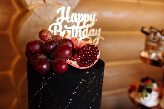 big black birthday cake with fresh fruits and sweets on a festive table. Candy bar. Table with different sweets for party.