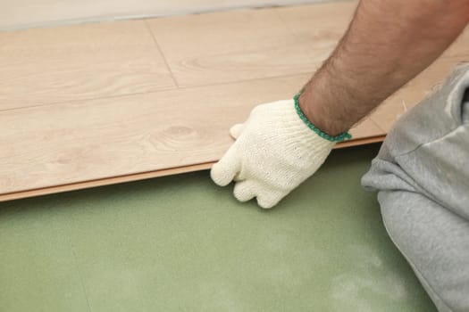 Installing laminate or parquet floor in room, detail on man hands fitting wooden tile, over green foam base.