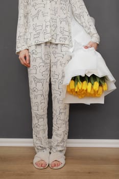 cropped photo of young woman holding big and beautiful blossoming bouquet of fresh yellow tulips flowers on the grey wall background at home. International Women's Day.