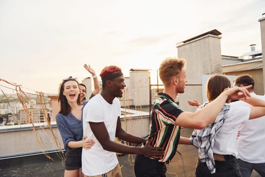 Recreation time. Group of young people in casual clothes have a party at rooftop together at daytime.