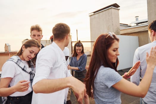 Recreation time. Group of young people in casual clothes have a party at rooftop together at daytime.