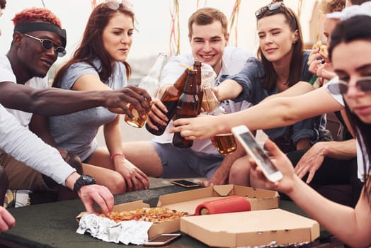 Delicious pizza. Group of young people in casual clothes have a party at rooftop together at daytime.