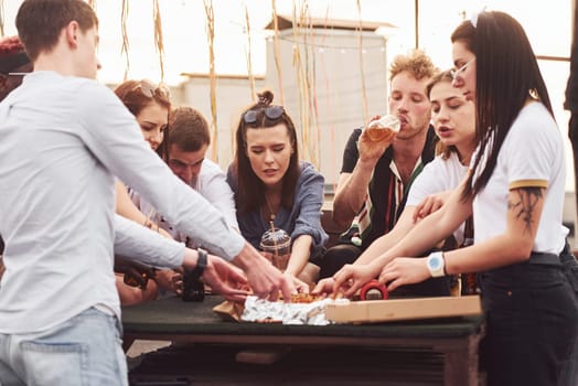 Delicious pizza. Group of young people in casual clothes have a party at rooftop together at daytime.