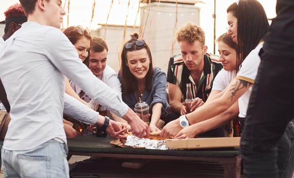 Delicious pizza. Group of young people in casual clothes have a party at rooftop together at daytime.