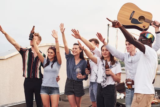 Group of young people in casual clothes have a party at rooftop together at daytime.