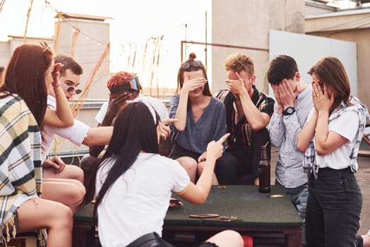 Playing game. Group of young people in casual clothes have a party at rooftop together at daytime.