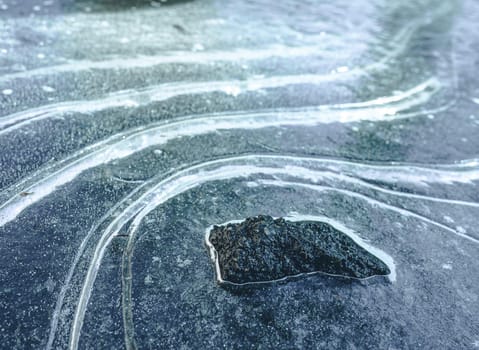 Dark, rugged rock formation standing amidst frozen landscape of icy curves and snow. Contrast of black, white, and blue colors creates dramatic and desolate scenery, conveying raw beauty and challenges of remote and untamed wilderness. High quality photo