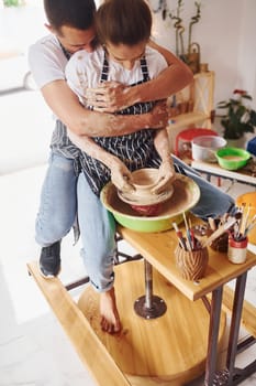 With her boyfriend or husband. Young female ceramist indoors with handmade clay product. Conception of pottery.