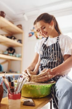 With her boyfriend or husband. Young female ceramist indoors with handmade clay product. Conception of pottery.