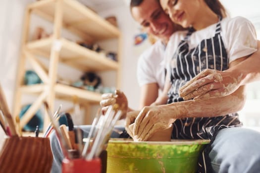 With her boyfriend or husband. Young female ceramist indoors with handmade clay product. Conception of pottery.