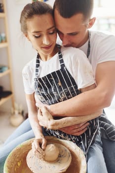 With her boyfriend or husband. Young female ceramist indoors with handmade clay product. Conception of pottery.
