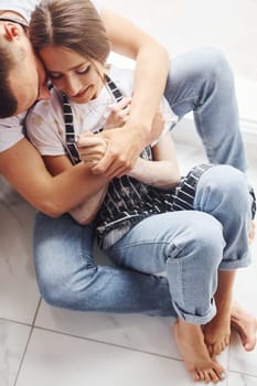 Cute young couple in jeans sitting down on the floor and embracing each other.