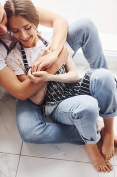 Cute young couple in jeans sitting down on the floor and embracing each other.