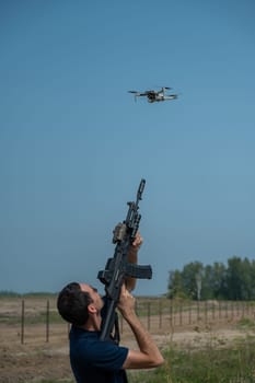 A man aims to shoot a rifle at a flying drone against a blue sky