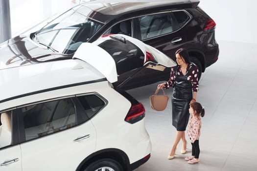 Mother with her daughter walking together near modern automobile indoors.