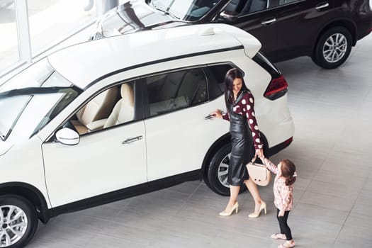 Mother with her daughter walking together near modern automobile indoors.