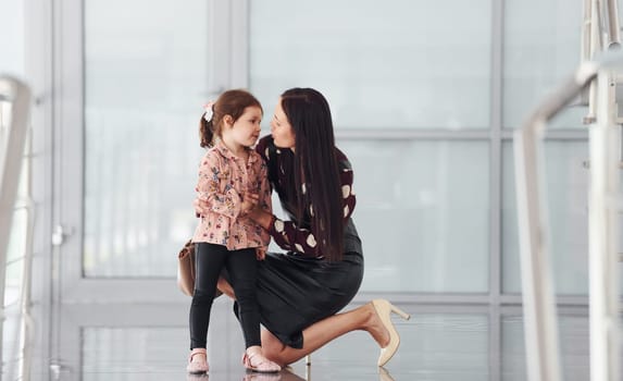 Young mother with her daughter walking together indoors in the office or airport. Having vacation.