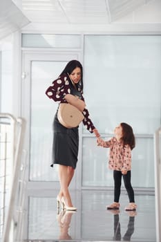 Young mother with her daughter walking together indoors in the office or airport. Having vacation.